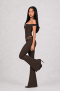 Woman wearing a brown off-shoulder top and flared pants on a light gray background
